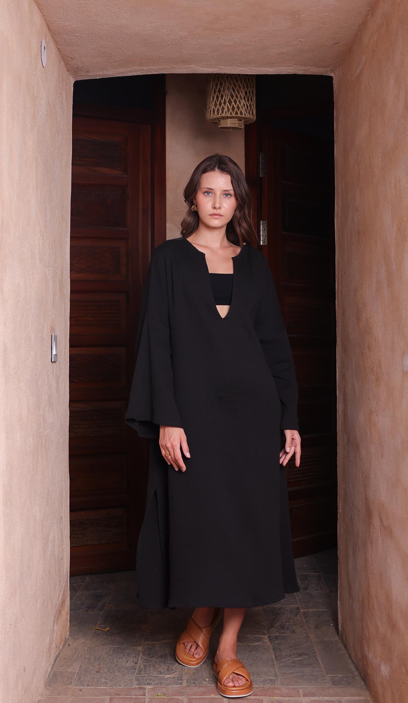 A woman in a flowing black Kiaan Kaftan from Thr3letter, featuring seersucker and organic cotton fabric.