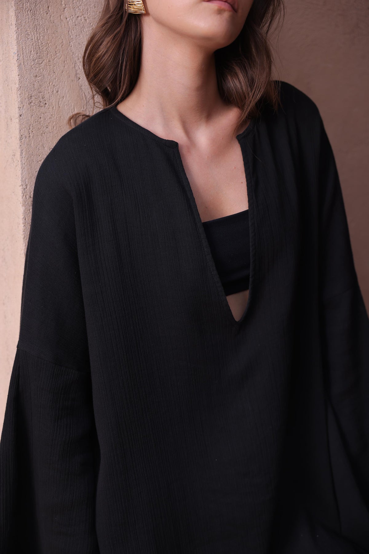 A woman models the Thr3letter Kiaan Kaftan in a sophisticated regal black, standing in a doorway.