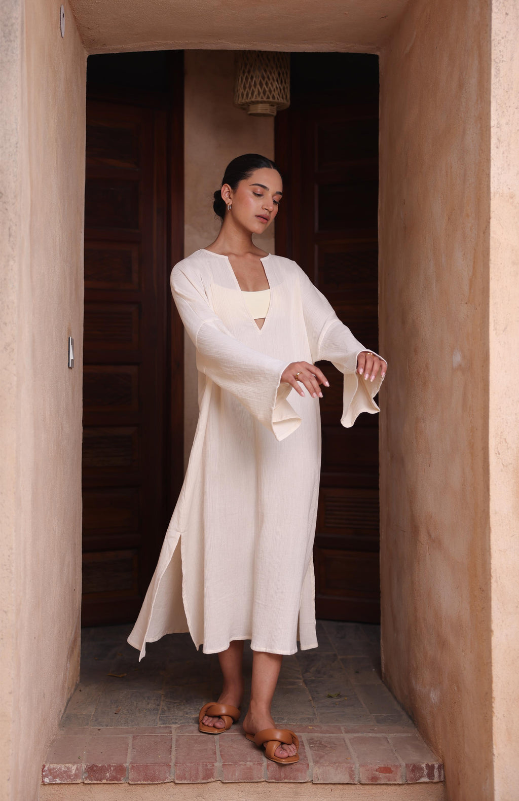 A woman wears Thr3letter's Kiaan Kaftan in a warm almond shade, creating a serene, tranquil atmosphere.