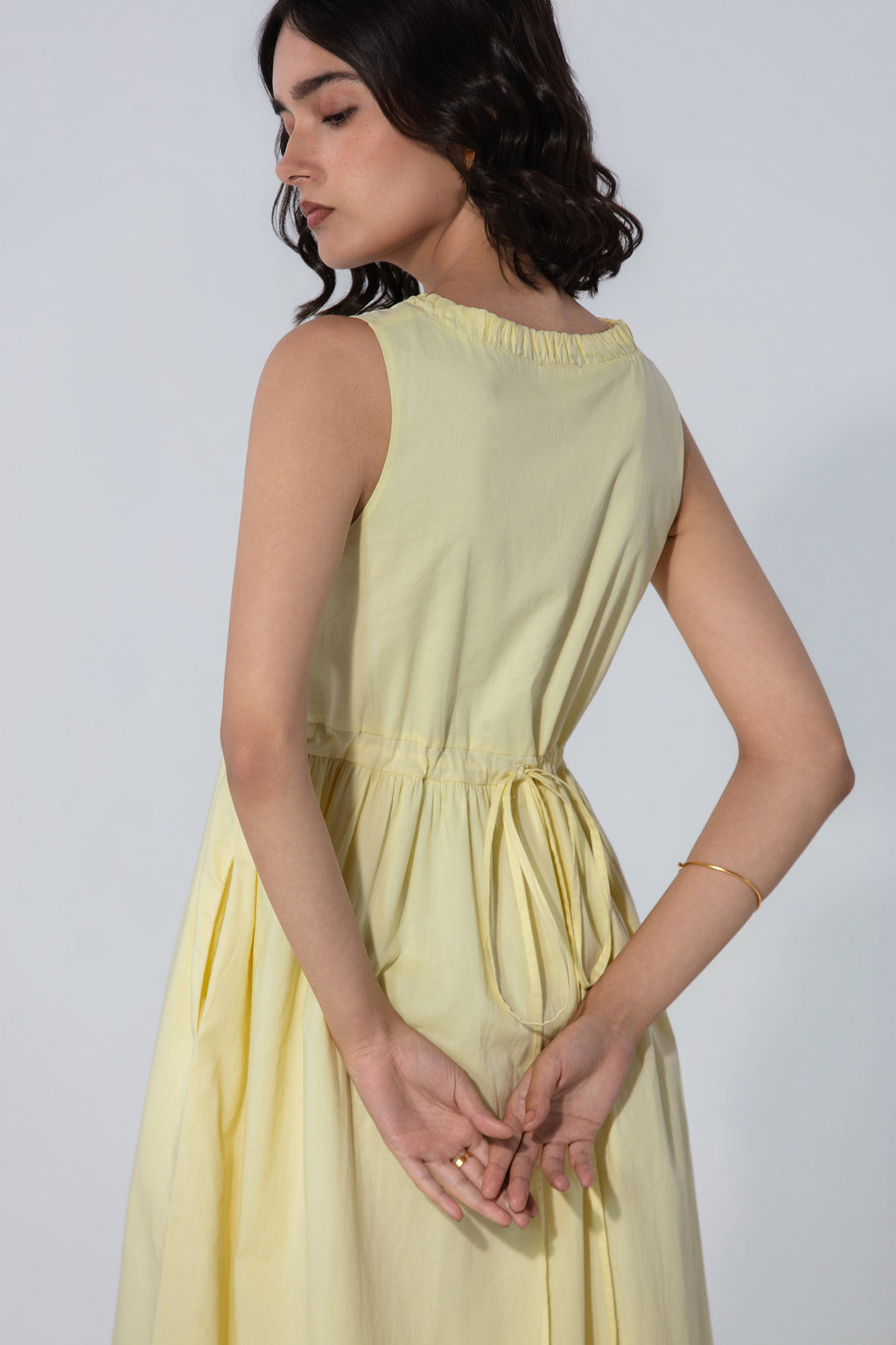 Back view of a pastel yellow sleeveless midi dress featuring an adjustable waist tie, gathered neckline, and flowy A-line silhouette.